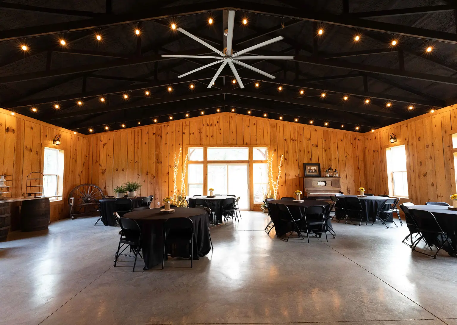 The farm event barn with string lights, round tables, and pine walls